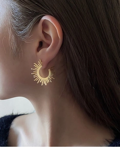 Close-up of a gold sunburst ear cuff earring with spikes on a female model