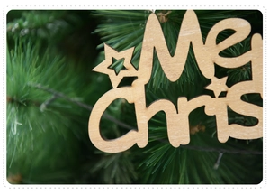 Close-up of laser-cut wooden Merry Christmas sign with stars on green pine background