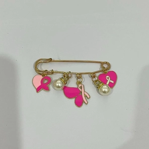 Détail de breloques cœur ruban rose et perles sur une broche épingle à nourrice dorée