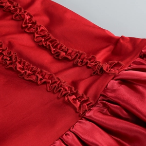 Detail eines roten Satinkleides mit Rüschensaum und geschichteten Raffungen im Stoff