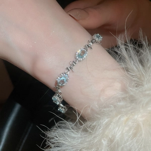 Macro shot of a silver bow bracelet featuring aquamarine zircons on a model wrist