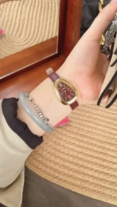 Close-up of a gold snake-head watch with red leather strap worn on a model's wrist