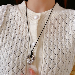 Close-up of geometric irregular silver pendant on a black cord over a white knit cardigan