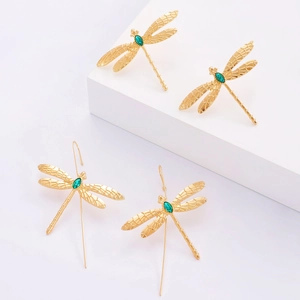 Gros plan sur des boucles d'oreilles libellule dorées avec pierres vertes sur socles