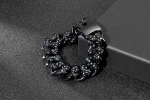 Close-up of a punk-style black stainless steel skull link bracelet on a matte black stand