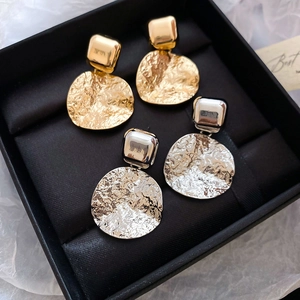 Detail of gold and silver geometric drop earrings with hammered metal texture in a box
