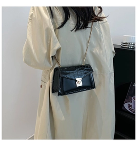 Detail of black crocodile texture bag with gold chain strap and metallic square lock