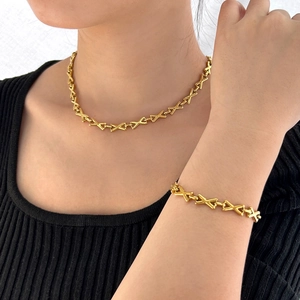 Close-up of gold-plated X-link chain necklace and bracelet set on a black top