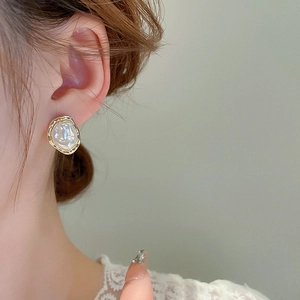 Close-up of elegant irregular baroque pearl earring with gold trim worn by a model