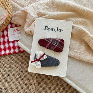 Detail of red plaid and lace bow hair clips on textured display card with natural props