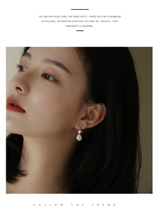 Close-up of elegant freshwater pearl drop earrings worn by a model with golden metal finish