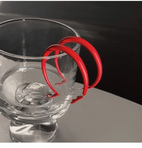 Macro view of matte red C-shaped hoop earrings hanging on a glass rim over dark background