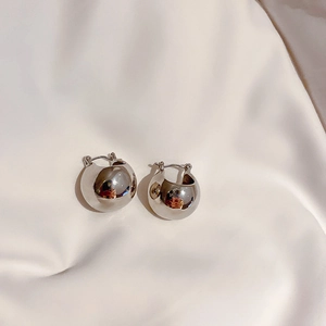 Detailed close-up of spherical silver stud earrings on soft cream satin fabric