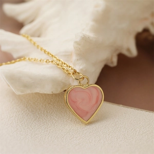 Golden chain necklace with pink marble heart pendant displayed on a white shell