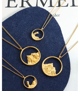 Detail of gold landscape relief pendants with mountain and wave motifs on blue felt