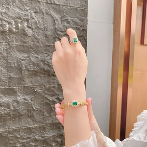 Detailed macro view of woven gold bracelet and matching emerald ring with diamond accents