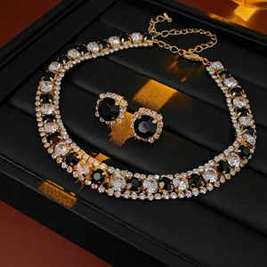 Detail of luxury necklace and earrings set with black and white crystals on black velvet