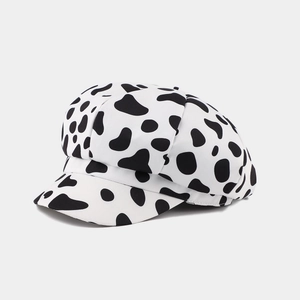 Detail view of the black and white cow print octagonal baker boy hat on white background