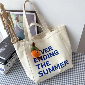 Detail of canvas tote bag with blue lettering and a cute orange persimmon plush charm
