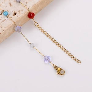 Detailed shot of a gold chain bracelet with colorful beads and butterfly charm on stone