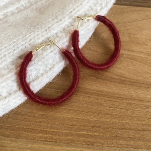 Close-up of burgundy flocked hoop earrings on a white knit fabric and wood background