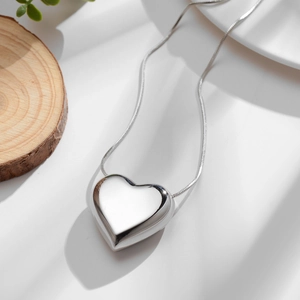 Minimalist silver 3D heart pendant necklace with polished snake chain on wood display