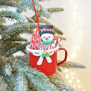Christmas snowman in red clay cup ornament hanging on snowy tree with warm festive lights