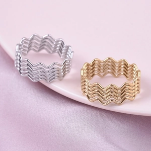 Polished wavy stainless steel rings in gold and silver finishes on a pink silk background