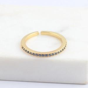 Detailed macro view of a gold open ring with micro-paved blue zircons on marble