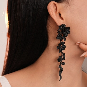 Close-up of elegant black flower leaf tassel earrings on female model with warm lighting