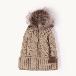 Detailed close-up of khaki chunky cable knit beanie with fluffy pom-pom and leather patch