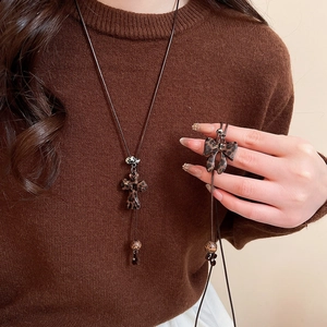 Détail des pendentifs croix et nœud à imprimé léopard sur une longue chaîne brune