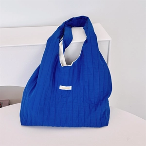 Macro shot of blue pleated fabric shoulder bag featuring a minimalist white label detail