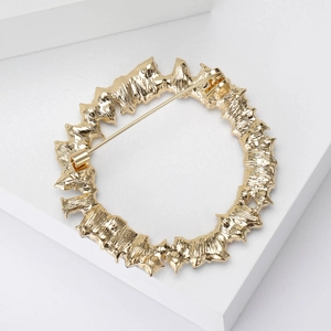Macro detail of gold wreath brooch showing sturdy safety pin clasp on a textured metal base
