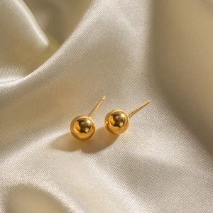 Minimalist polished golden spherical stud earrings displayed on beige silk fabric