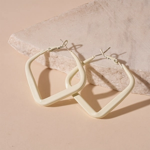 Close-up of geometric square cream enamel earrings leaning on a textured stone