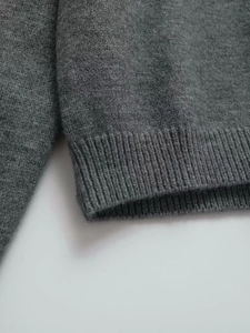 Detailed close-up of dark grey knit sweater showing ribbed hem and soft wool texture