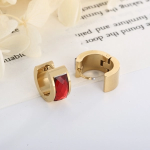 Detail of gold U-shaped earrings with red rectangular gemstone on elegant cream background