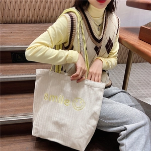 Detail of canvas tote bag featuring yellow smile embroidery and colorful beaded strap