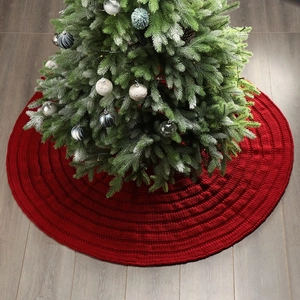 Detailed close-up of a red knitted Christmas tree skirt on a dark wood floor