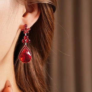 Close-up of a red teardrop crystal earring with vintage floral zircon detailing on a model