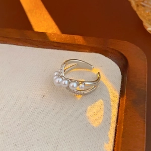 Detailed view of silver cross ring with pearls and zircons on a beige textured fabric