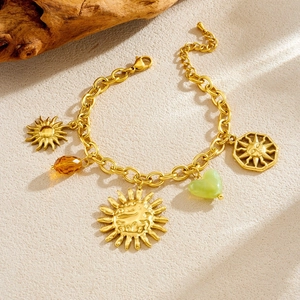 Golden sun charm bracelet with heart-shaped stone and tiger eye bead on textured background