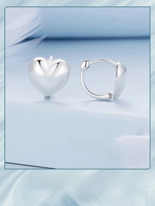 Elegant silver heart-shaped earrings on a blue surface with soft white feathers