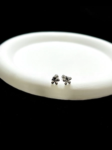 Macro detail of silver minimalist five-petal flower stud earring on white display