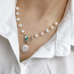 Close-up of pearl necklace with gold butterfly pendant and baroque drop on a model