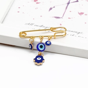 Detail of Hamsa hand and blue evil eye charms on a golden safety pin brooch