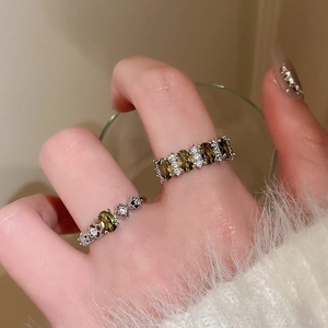 Detailed close-up of vintage oval green emerald rings with diamond accents on a finger