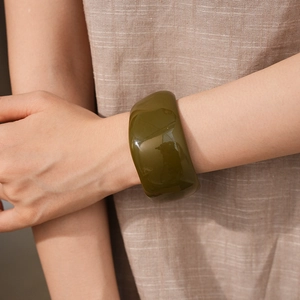 Close-up of a minimalist olive green resin wide bangle on model's wrist with linen fabric