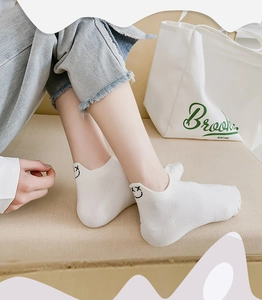 Close-up of white low-cut socks with minimalist black smiley face embroidery on the heel